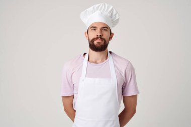 Beyaz önlüklü sakallı adam mutfağında yemek pişiriyor.