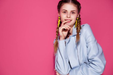 Mavi ceketli, saçları örgülü, parlak makyajlı, pembe arka planlı çekici bir kadın.