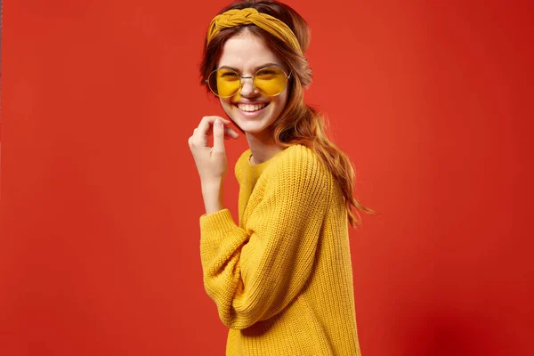 Hezká žena ve žlutém svetru brýle módní emoce červené pozadí — Stock fotografie