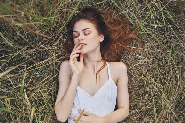 Uma mulher de vestido branco jaz na grama com os olhos fechados descansando o sol — Fotografia de Stock