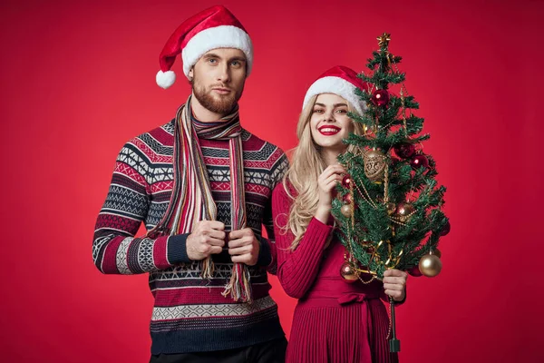 Άνδρας και γυναίκα στέκεται δίπλα στο χριστουγεννιάτικο δέντρο παιχνίδια lifestyle κόκκινο φόντο — Φωτογραφία Αρχείου