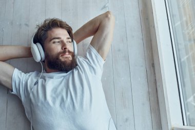 Sakallı adam pencerenin kenarında uzanmış, kulaklık takıyor.