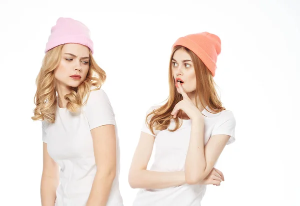 Δύο γυναίκες σε λευκό t-shirts καπέλα στο κεφάλι φως επικοινωνίας μόδας φόντο — Φωτογραφία Αρχείου