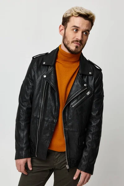 Hombre rubio de moda en una chaqueta de cuero negro y un suéter naranja inclinó su cabeza hacia un lado —  Fotos de Stock