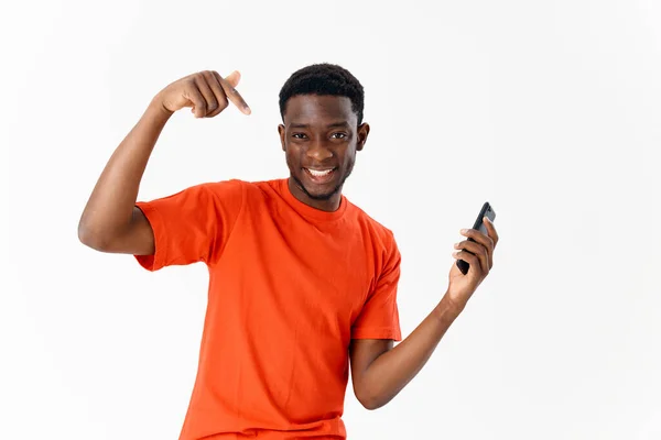 Homem alegre de aparência africana com um telefone em suas mãos gesticulando com um fundo de luz do dedo — Fotografia de Stock