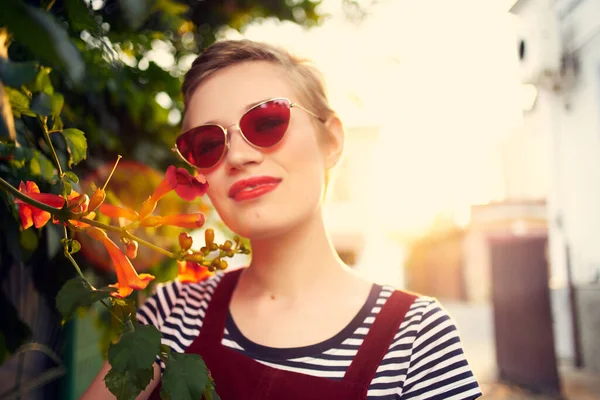 Vacker kvinna bär solglasögon buske med blommor utomhus — Stockfoto