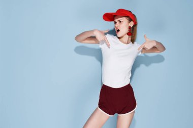 Tişörtlü ve şortlu neşeli güzel kadın. Yazlık kıyafetler, mavi arka plan.