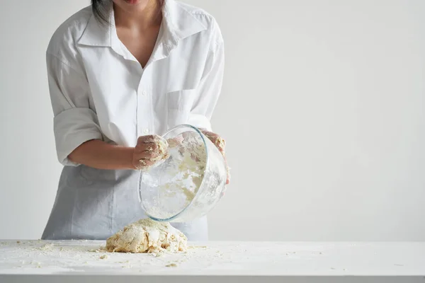 Kobieta w kucharzy mundurowych ugniata ciasto na stole mąka światło tła — Zdjęcie stockowe