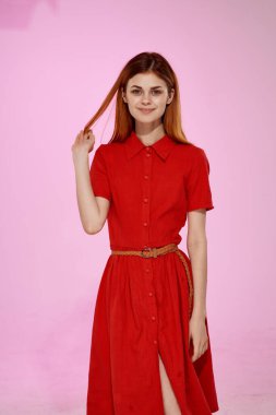 Kırmızı elbiseli kızıl saçlı kadın. Çekici poz veriyor. Pembe arka plan.