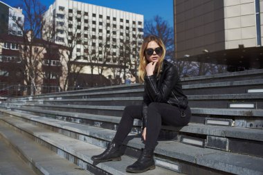 Deri ceketli kadın açık hava tatili için bina yakınında.