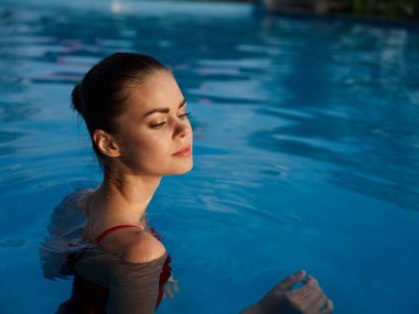 Havuzda lüks bir tatilde gözleri kapalı çekici bir kadın.