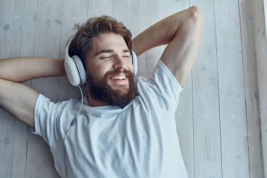 Sakallı adam pencere eşiğinde uzanıyor, kulaklık takıyor.