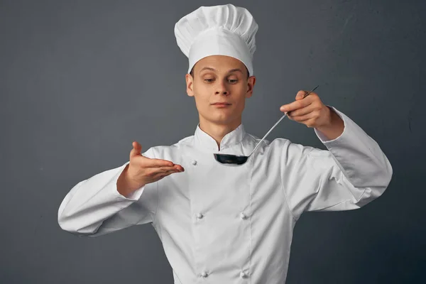 a chef with a cap on his head a scoop in his hands cooking food dark background