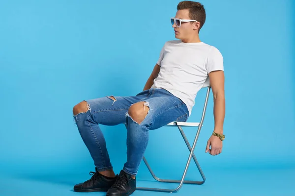 Un uomo si siede su una sedia in una t-shirt bianca in stile moderno posa — Foto Stock