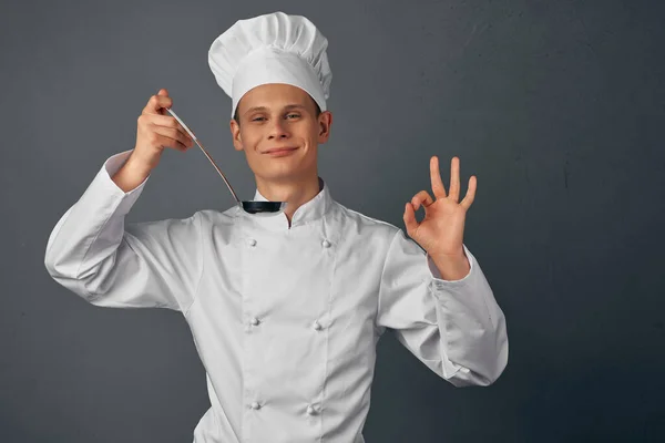 Maschio chef con un mestolo in mano sta cercando piatti ristorante professionale — Foto Stock