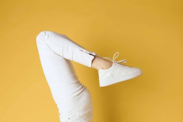 Женские перевернутые ноги в белых кроссовках обрезанный вид на желтый фон — стоковое фото