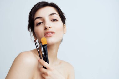 Ellerinde makyaj malzemeleri olan çıplak omuzları ve cilt bakımı olan bir kadın.