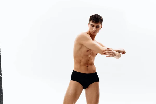 Uomo con corpo nudo muscolare nel buio in pantaloncini vista ritagliato in background luce — Foto Stock