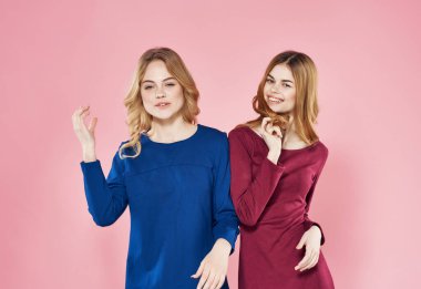 Elbiseli şirin kızlar pembe arka planda yan yana duruyorlar.