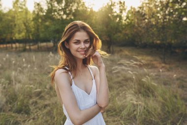 Yeşil çim tarlasında yürüyen beyaz elbiseli neşeli güzel kadın.