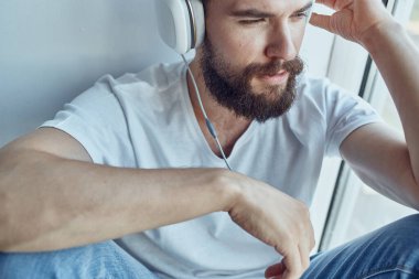 Kulaklıklı bir adam pencerenin yanında oturmuş kulaklıkla müzik dinliyor.