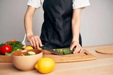 Siyah önlüklü kadın mutfakta sebze doğruyor ve yemek hazırlıyor.