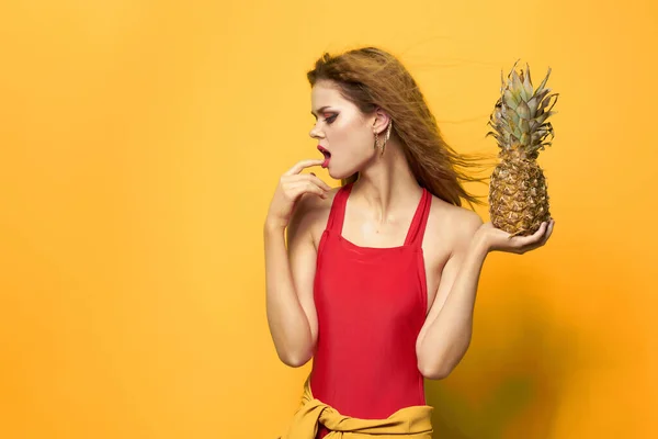 Kvinna i röd t-shirt med ananas i händerna exotisk gul bakgrund — Stockfoto