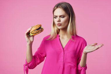 Pembe gömlekli neşeli kadın hamburger diyeti yapıyor.
