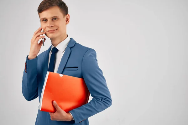 Un uomo in giacca e cravatta con una cartella rossa un telefono tra le mani con tecnologia di comunicazione — Foto Stock