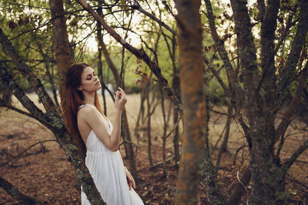 Woman in white dress leaning on a tree in forest