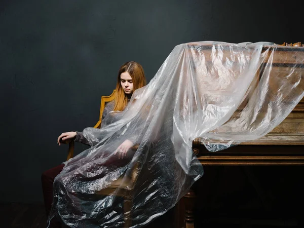 피아노 옆 의자에 앉아 있는 한 여자가 폴리에틸렌의 어두운 배경에 앉아 있다 — 스톡 사진