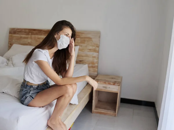 Podrážděný žena na sobě lékařská maska sedí na posteli uvnitř hotelu dovolená karanténa izolace — Stock fotografie