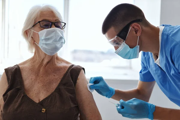 male doctor giving an injection to an elderly woman patient vaccine passport hospital