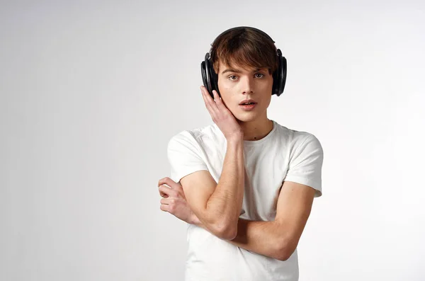 Chico en camiseta blanca con audífonos música tecnología fondo claro — Foto de Stock
