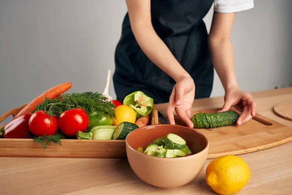 Ama de casa en un delantal negro en la cocina cocina cocina vitaminas ensalada —  Fotos de Stock
