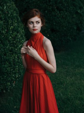 Kırmızı elbiseli kadın. Parlak makyaj dekorasyonu yeşil çalılık.