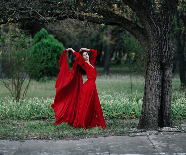 Woman in red dress near tree green grass nature posing. High quality photo