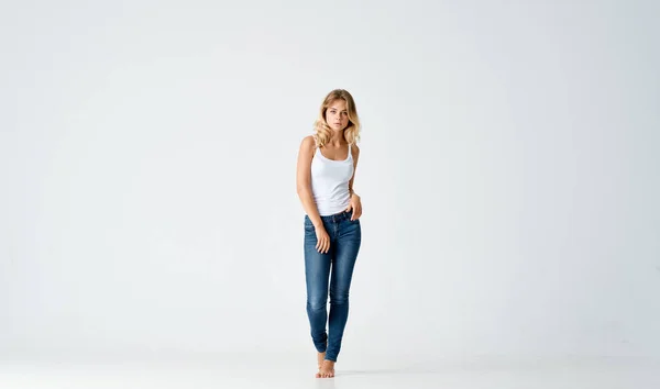 Hezká blondýna v džínách bosá představuje módní izolované pozadí — Stock fotografie