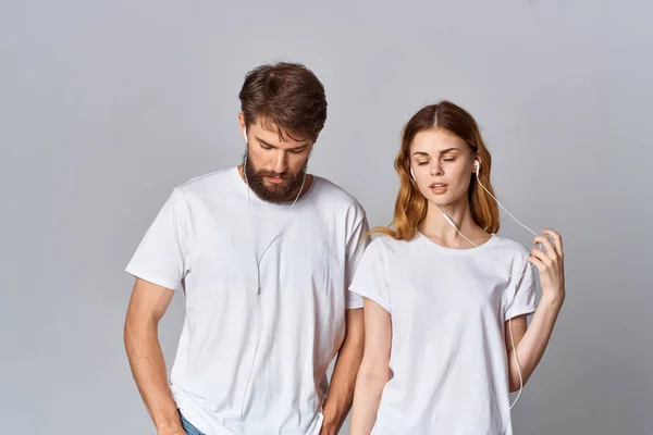 Muž a žena v bílé trička hudba ve sluchátkách světlo pozadí — Stock fotografie