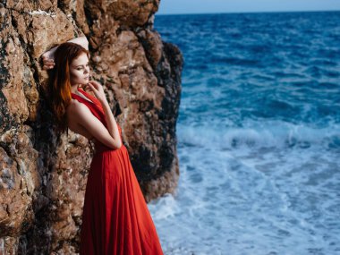 Kırmızı elbiseli güzel bir kadın lüks okyanus sahili yaşam tarzıyla poz veriyor.