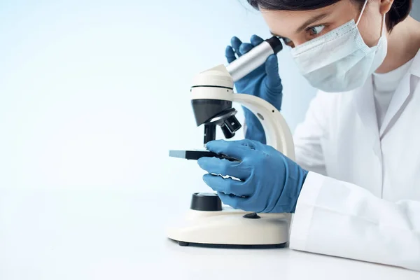 Γυναίκα βοηθός εργαστηρίου σε μια ιατρική μάσκα κοιτάζοντας μέσα από μια έρευνα μικροσκόπιο — Φωτογραφία Αρχείου