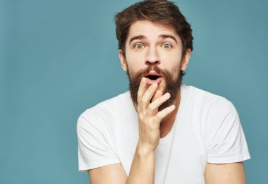 Beyaz tişörtlü bir adam mavi arka planda öfke hareketi yapıyor.