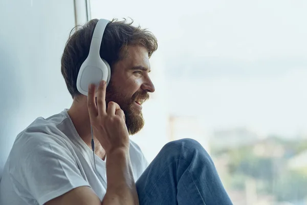 Homme assis sur le rebord de la fenêtre dans les écouteurs dans la mode casque — Photo