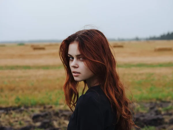 Mujer en vestido negro en el campo pelo rojo posando resto — Foto de Stock