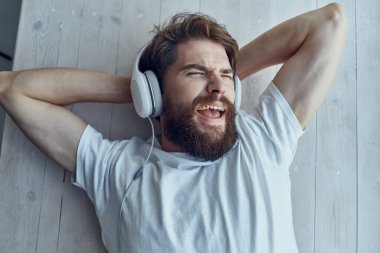 Sakallı adam pencerenin kenarında uzanmış, kulaklık takıyor.