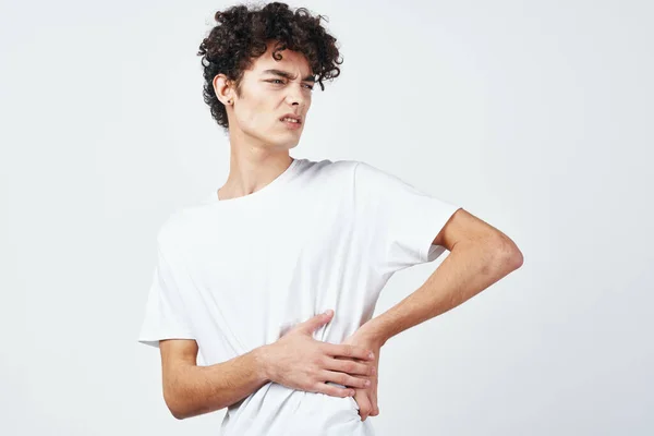 Cara encaracolado em uma camiseta branca segurando seu desconforto diarréia estômago — Fotografia de Stock