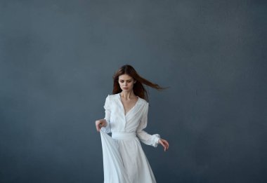 Güzel kızıl saçlı, beyaz elbiseli, eğlenceli dans eden, siyah arka planlı bir kadın.