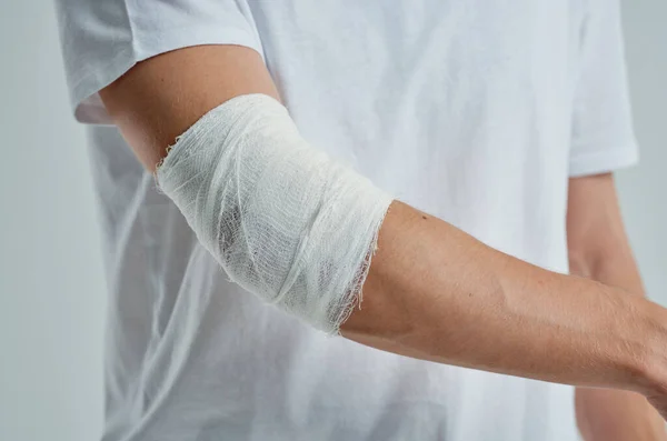 Hombre enfermo en una camiseta blanca con un fondo ligero de mano vendado —  Fotos de Stock