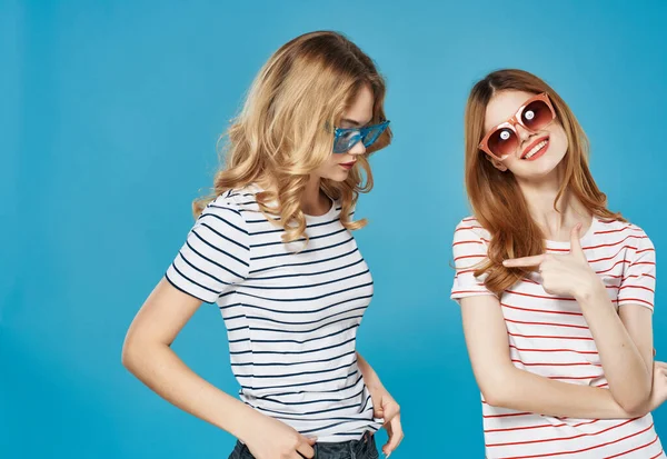 티셔츠를 입고 화려 한 안경 엔터 테인 먼 트 글래머, 파란 배경을 가진 두 여자 친구 — 스톡 사진