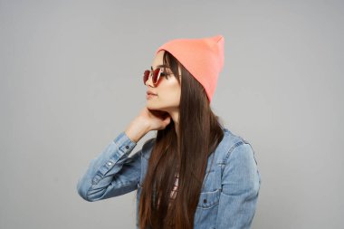 Kot gömlekli güzel kadın güneş gözlüklü pembe şapkalı moda gri arka plan stüdyosu.